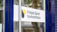 Pohjois-Savon hyvinvointialueen kyltti ovessa.