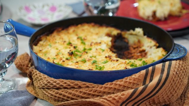 En blå gjutjärnspanna med en paj med gratinerat potatismos på toppen.