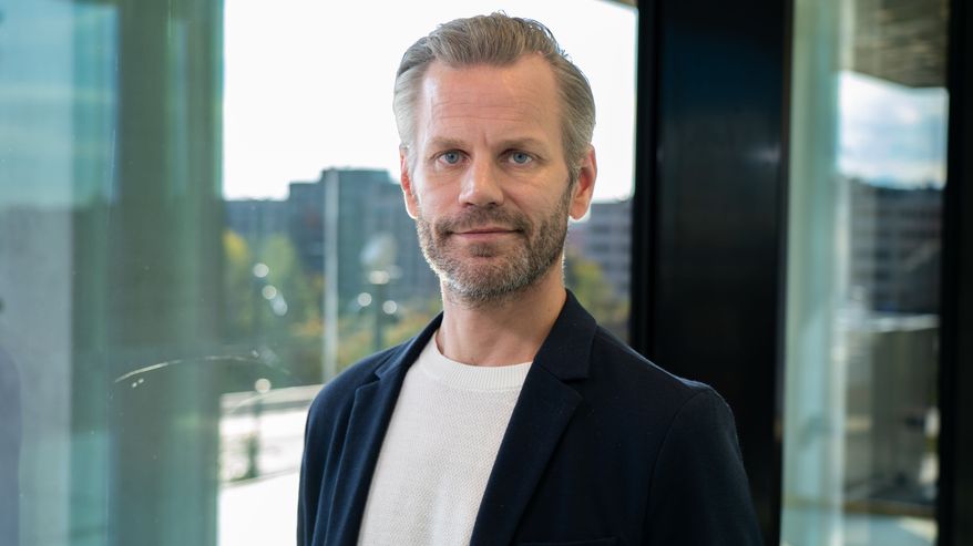 En man iklädd kavaj fotograferad framför ett fönster.