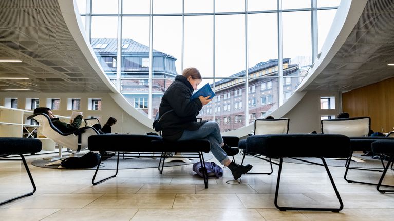 Two people reading in a modern university library with a large curved window. 