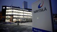 En Wärtsilä-skylt framför en upplyst byggnad med glasfasad i vinterlandskap.