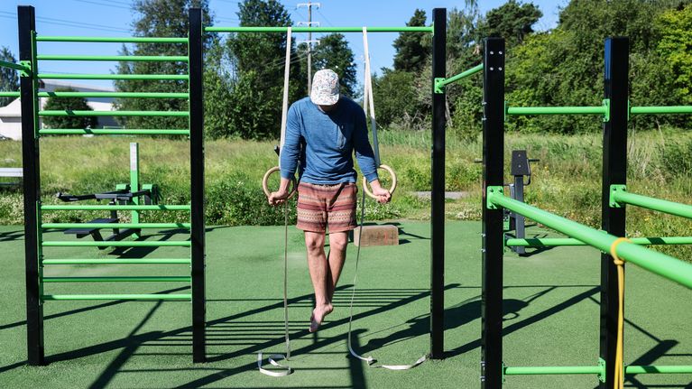 Lippispäinen mies roikkuu renkaissa ulkokuntosalilla.