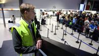 Keltaiseen huomioliiviin pukeutunut mies katselee portailta alapuolella olevaa lentoaseman lähtöselvitystä jossa ruuhkaa.
