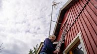 Man som står på en stege och ser ner mot kameran. En röd husvägg och en tv-antenn  i bakgrunden.