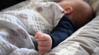 Vauva nukuu käsi nyrkissä, käsi kuvan etualalla taustalla näkyy hämyisesti vauvan korva peiton alta.