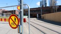 Etualalla liikkumisen kieltävä kyltti, taustalla ratikkakiskot ja tumma rakennus. 