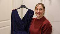 En kvinna i röd tröja, Anette Karlsson, håller upp en mörkblå balklänning med glitter.