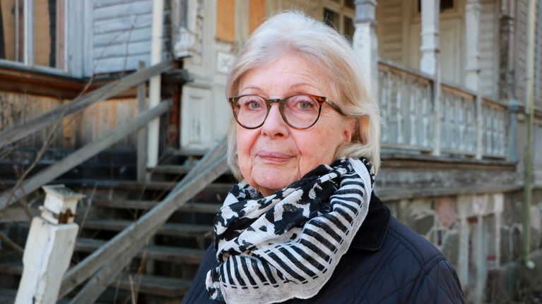 Kvinna framför gammalt trähus.