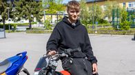 En tonårig pojke sitter på sin moped på skolans gård. 