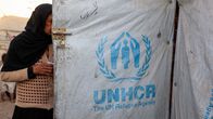 Jemeniläinen pakolaisnainen menossa sisään tilapäismajoitteeseen, jonka pressusta rakennetussa seinässä on UNHCR:n logo.