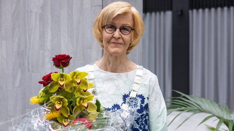 Päivi Hietanen, uusi arkkiatri, katsoo kameraan kukkia kädessään.