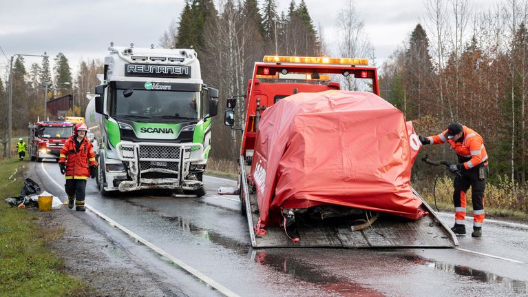 Onnettomuuspaikalla rekka, jonka etukulma on rutussa. Hinausauton kyytiin nostettu, pressulla peitetty henkilöauto. Pelastushenkilöstöä.