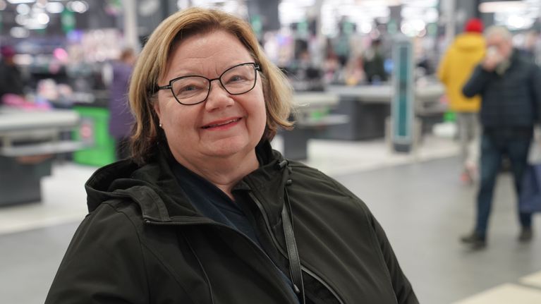Virpi Hemmer jouluostoksilla hymyilee kassarivistön edessä Kaaren kauppakeskuksessa.