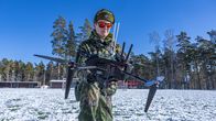 Aurinkolasipäinen varusmies pitelee mustaa droonia käsissään. 