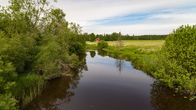 Looking down a small river, with trees and fields and a small red house in the background.