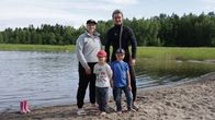 Två vuxna och två barn står på en sandstrand, med skog i bakgrunden.
