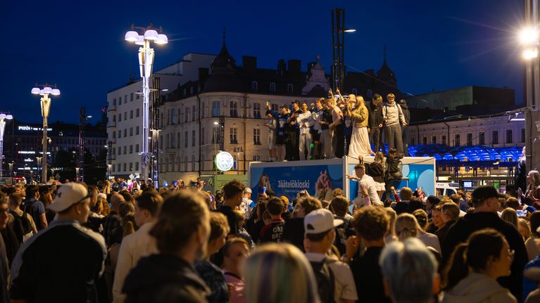 Nuoria seisomassa Keskustorin jäätelökioskin päällä. Keskustori on täynnä ihmisiä.