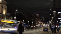 Yökuva kaupungista, jossa katuvalot valaisevat tietä. Etualalla henkilö seisoo kadulla, ja taustalla näkyy liikkuvia autoja ja rakennuksia, joiden valot luovat elävän tunnelman.