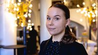 Aurora Idänpää katsoo puolilähikuvassa kameraan ja hymyilee. Taustalla näkyy hotellin aulaa ja kirkkaita lämpimänsävyisiä valoja.