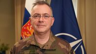 Pierre Vandier, NATO:n ACT:n komentaja seisoo Suomen ja NATO_lipppujen edessä kameraan katsoen.
