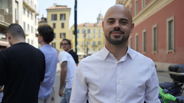 Ung man i vit skjorta tittar leende in i kameran på en gata i Milano.