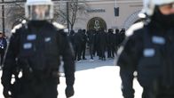 Poliiseja etualalla, mustiin pukeutuneita mielenosoittajia taustalla.
