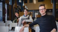 Kolme nuorta miessoittajaa istuu musiikkisalin katsomossa, kahdella on sylissään sello.