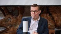 En man med glasögon och blå kavaj sitter vid ett bord.