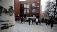 Demonstration utanför en byggnad i ett stadsområde. En grupp människor samlas med skyltar och banderoller.