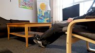 En människa sitter i en stol, man ser bara personens ben och fötter samt ena armen. 