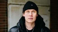 Henkilö mustassa untuvatakissa ja mustassa pipossa katsoo kameraan.