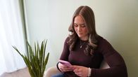 Personen sitter i en stol och håller i en rosa mobiltelefon. 