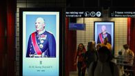 Metroaseman käytävällä seinällä on muotokuva H.M. Kong Harald V:stä, alla teksti "1937–2024". Taustalla kulkee ihmisiä.