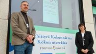 En man, Jarkko Vainionpää, i kavaj står framför ett fönster tillsammans med Marjo Rantala, chef för idrottstjänster i Borgå. 