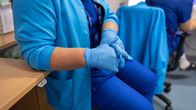 A nurse sitting with her hands in her lap, wearing rubber gloves.