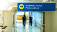 Skylt till patientombudsmannen, två blåklädda sköterskor går i bakgrunden