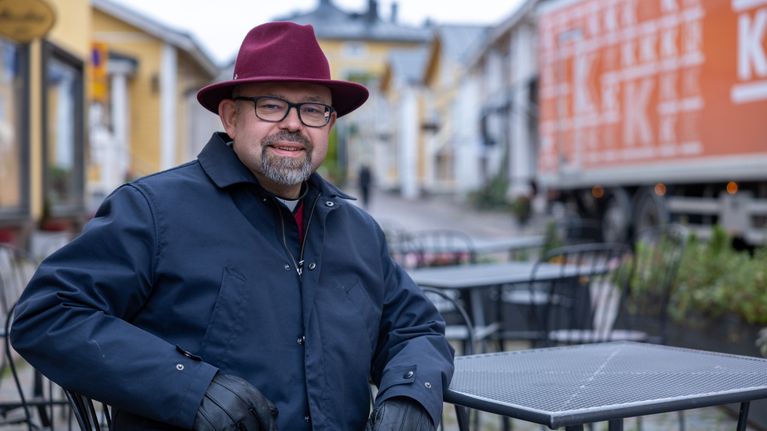 En man i prästkrage och hatt sitter på ett café.