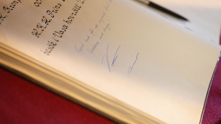 Uppslagen gästbok med handskriven text och två namnteckningar på sidan, penna synlig upptill till höger.