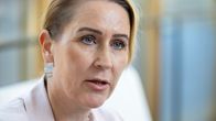 Nainen vaaleassa bleiserissä katsoo eteenpäin. Taustalla näkyy epätarkkaa sisätilaa.