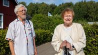 Pentti Arajärvi ja Tarja Halonen seisovat soratiellä pensasaidan vieressä, taustalla suomalainen lippu ja punainen puurakennus.