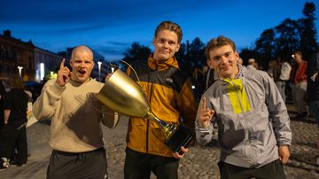 Kolme miestä poseeraa leikkipokaali kädessään kameralle.