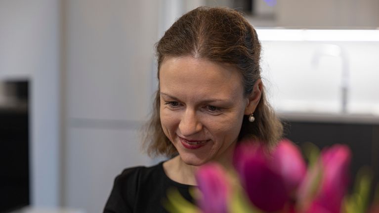 Nainen istuu keittiössä pöydän ääressä, etualalla tulppaaneja maljakossa.