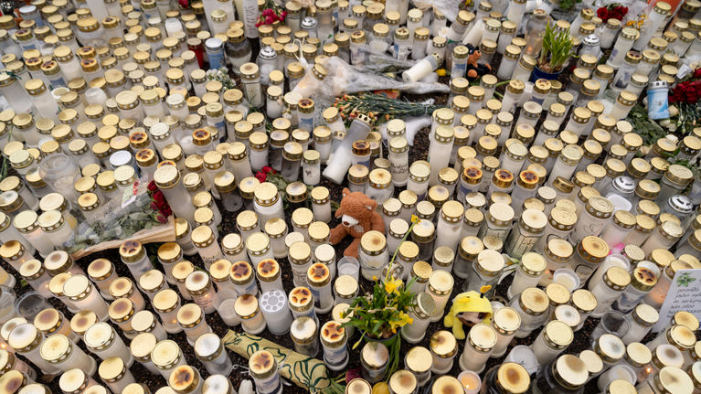 Grave candles, soft toys, flowers and cards on the ground.