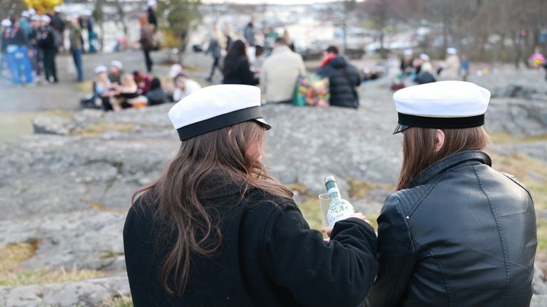 Two young women wearing white student caps sit in a park.