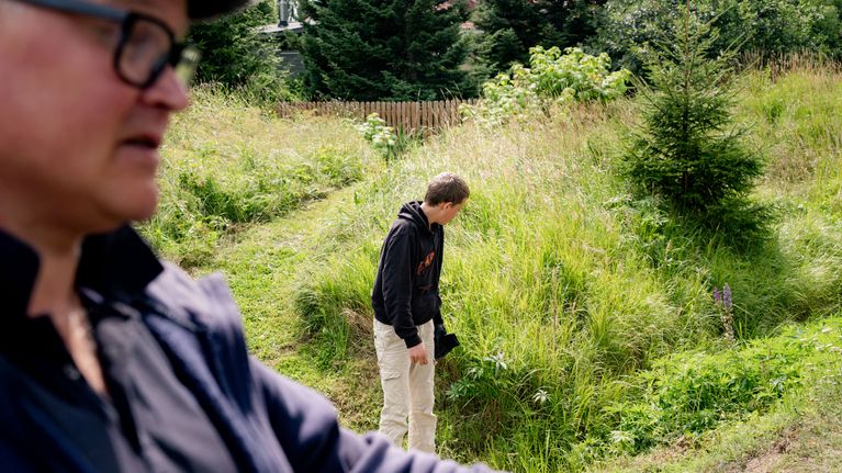 Två personer står vid en äng och tittar in i buskaget.