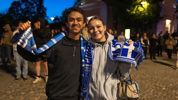 Nuori mies ja nuori nainen poseeraavat iloisena kauloissaan Suomi-kaulahuivit.