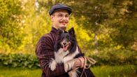 Mies katsoo kameraan hymyillen koira sylissään.
