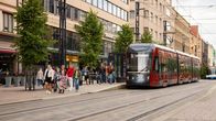 Ratikka pysähtyneenä pysäkille Tampereen Hämeenkadulla. Ihmisiä kävelee poispäin pysäkiltä.