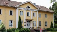 Gul trävilla med skylten "Sagalundgården" ovanför entrén, omgiven av grönska och grusplan framför huset.