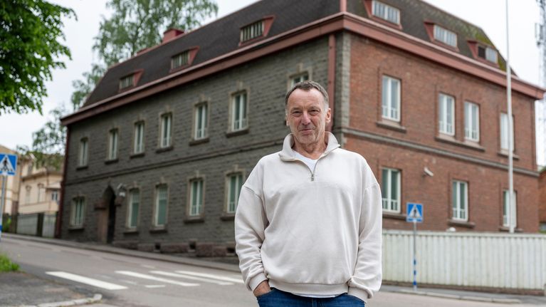 Theodor Steidel står i ljus tröja och jeans framför Lovisa gamla polishus, en gammal byggnad i rödtegel.